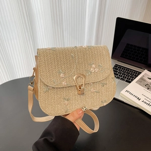 Straw crossbody bag with floral embroidery and gold metal lock in a stylish office setting