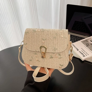 Straw crossbody bag with floral embroidery and gold U-shaped buckle on a desk