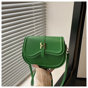 Close-up of green leather saddle bag featuring a prominent gold H-shaped metal buckle