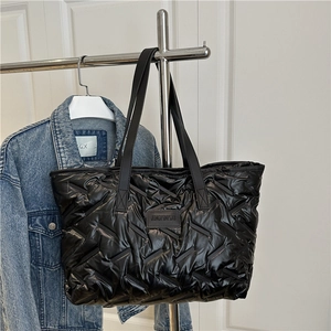 Minimalist black quilted tote bag with woven straps and glossy padded nylon finish