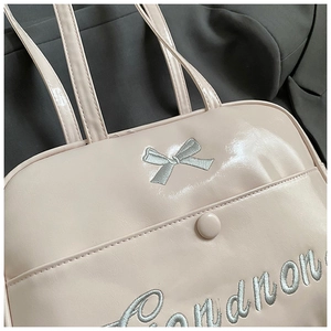 Close-up of pink glossy PU leather bag with embroidered bow and silver lettering details