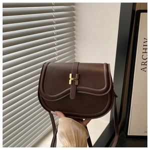 Detail view of dark brown leather saddle bag featuring a vintage golden H-buckle closure