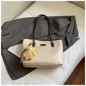 Detail of cream tote bag with coffee edges, featuring a plush bear and fashion plaque