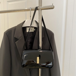 Minimalist black patent leather shoulder bag with gold clasp on a gray background