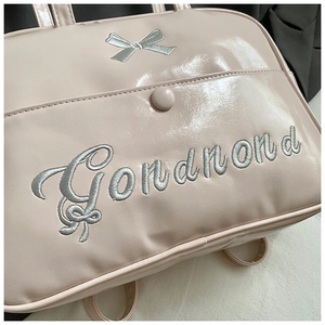 Detail of pink glossy faux leather shoulder bag with silver bow embroidery and script text