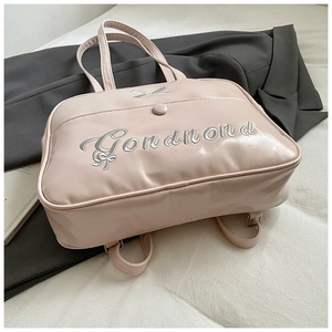 Detail of pink glossy PU handbag featuring silver metal bow and cursive embroidery