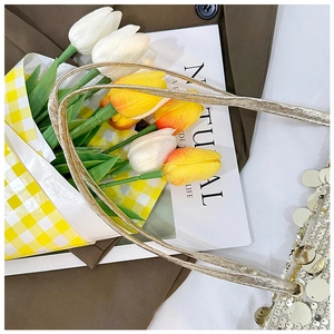 Detail of shimmering silver sequin tote bag next to tulips and a brown autumn coat