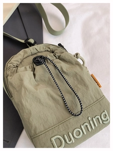 Detail of olive green nylon crossbody bag with embroidered logo and drawstring closure