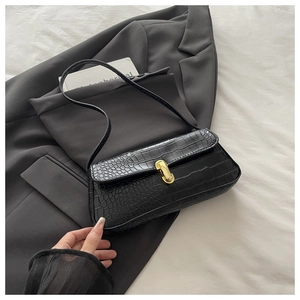 Detail of black crocodile texture leather underarm bag with gold buckle on grey blazer