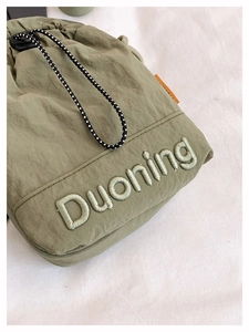 Detail of olive green nylon bag featuring Duoning embroidery and checkered drawstring