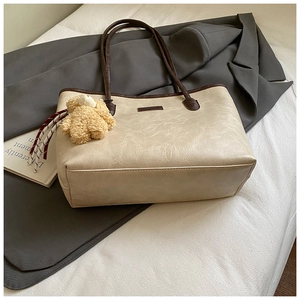 Detail of beige tote bag with pleated texture, brown handles and cute plush bear charm
