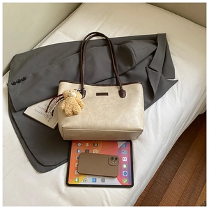 Close-up of beige tote bag with brown straps and cute bear charm on a white bed