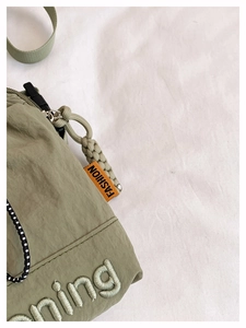 Detail of light green nylon crossbody bag with orange fashion label and embroidery