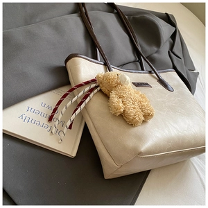 Detail of beige faux leather tote bag with brown handles and cute plush bear charm accessory