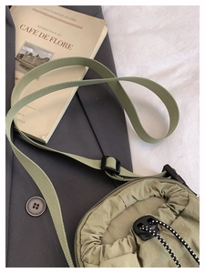 Olive green nylon drawstring crossbody bag shown on grey blazer with vintage books