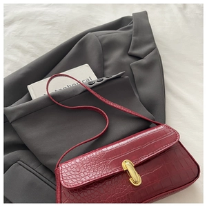Close-up of wine red faux crocodile leather shoulder bag with gold oval metal clasp