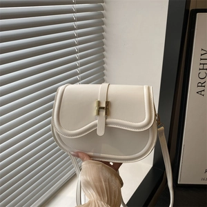 Elegant cream saddle bag with gold H-shaped buckle shown in minimalist interior setting