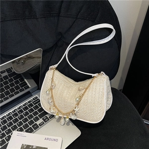 Sac sous le bras blanc tressé avec chaîne dorée à perles et coquillages sur fond texturé noir