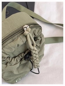 Detail of sage green drawstring crossbody bag with pleated texture and embroidery