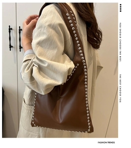Detail of a brown leather hobo bag featuring dense silver stud rivets and a sleek strap