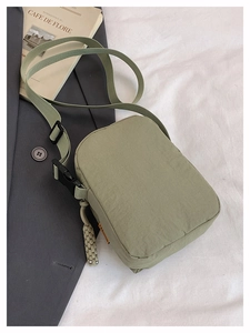 Detail of sage green nylon crossbody bag with adjustable strap and orange label accent