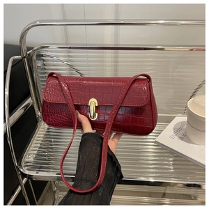 Detail of burgundy crocodile-embossed leather underarm bag with gold oval buckle