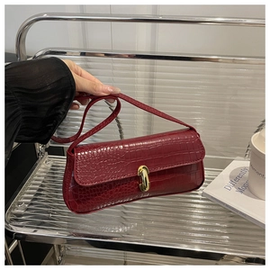 Detail of burgundy crocodile pattern leather bag with elegant golden twist-lock closure