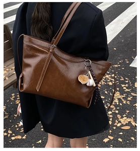 Detailed view of brown tote bag with baseball charm and textured leather on a street