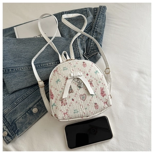 Detail of white mini backpack with pink rabbit pattern and heart pendant next to a phone