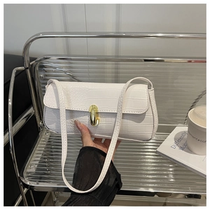 Detailed view of white crocodile pattern baguette bag with gold buckle held by a model