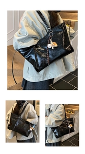 Detail view of large black shiny tote bag with baseball charm on shoulder strap