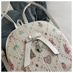 Close-up of white embossed backpack with cartoon prints and metallic heart pendant