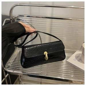 Close-up of black crocodile embossed faux leather baguette bag with gold metal buckle