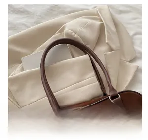 Detail of dark brown suede handbag with slim straps and silver rings on white blazer