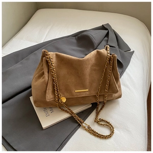 Detailed close-up of brown suede handbag featuring gold chain and minimalist metal bar