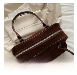 Detail of dark brown suede handbag with silver zipper and fine handles on neutral background
