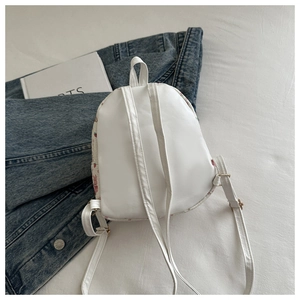 Flat lay of a white mini leather backpack with pink accents next to a denim jacket