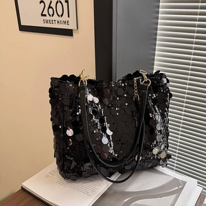 Elegant black sequin crossbody tote bag with gold hardware on a wooden table setup
