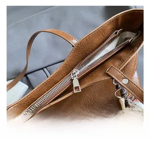 Close-up of brown textured leather tote bag featuring silver zipper and baseball charm detail