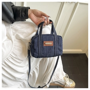 Detail of dark blue denim mini tote bag with brown leather patch and crossbody strap