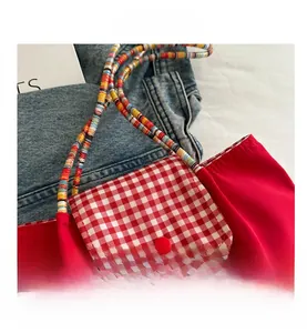 Close-up of red fabric shoulder bag featuring red plaid pocket and colorful woven strap