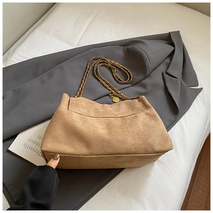 Detailed view of brown suede tote with gold chain strap on a stylish grey blazer background