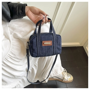 Detail of dark blue denim handbag with white stitching and leather metal tag