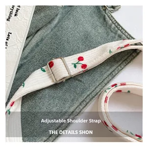 Dettaglio della tracolla regolabile in denim con stampa ciliegia rossa e fibbia metallica