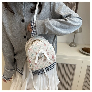 Mini white backpack with cartoon prints and silver heart pendant shown on model in a casual setting