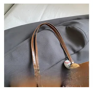 Detail of a brown glossy tote bag featuring metal rivets and a creative baseball charm