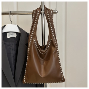 Close-up of brown faux leather tote bag featuring detailed silver rivet studs on the strap