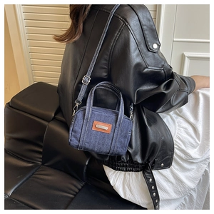 Detail of blue denim mini pillow bag with brown leather patch and white stitching on strap