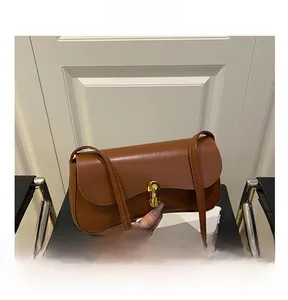 Close-up of a brown leather underarm bag featuring a gold metal twist-lock and slim strap