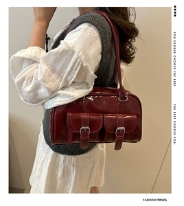 Close-up of glossy burgundy patent leather shoulder bag with decorative silver buckles
